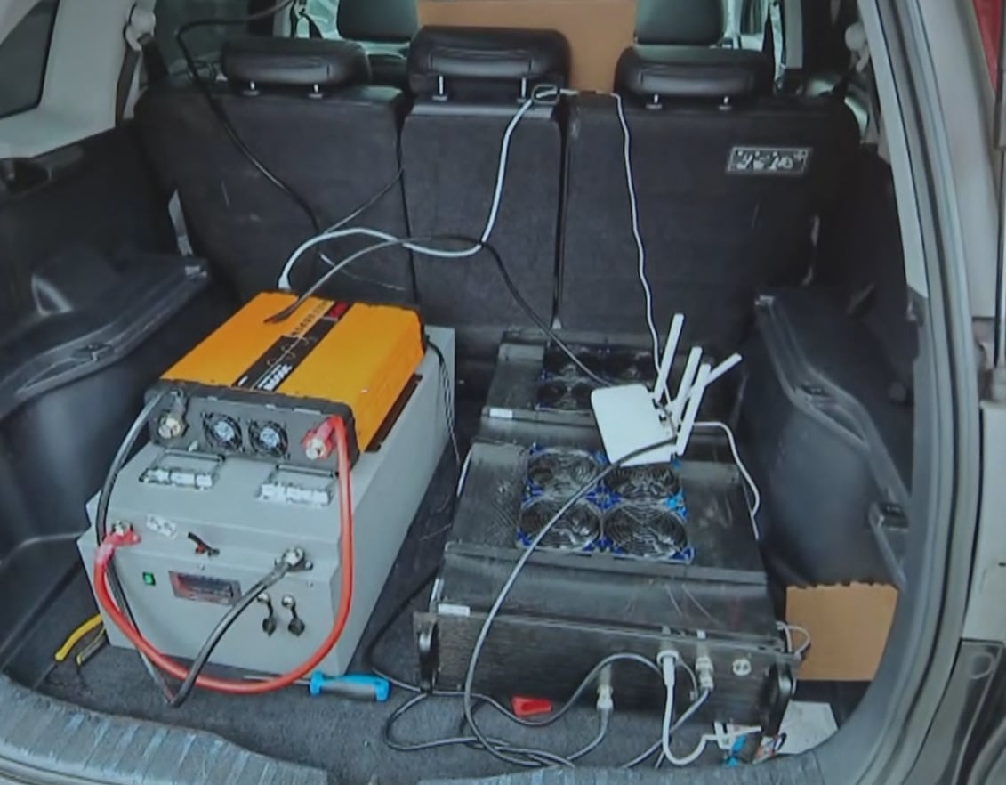 A trunk of a car shows two big electronic boxes inside used to mimic a cell tower and defraud victims by sending fraudulent text messages.