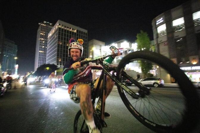 A cyclist pops a wheely biking down a street with other cyclists behind him.