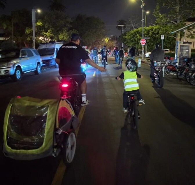 A man and a small child ride a bike on a street following a group of other cyclists.