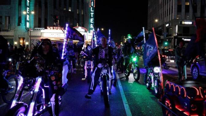 A group of cyclists with neon lights on their bikes ride down a street at night.