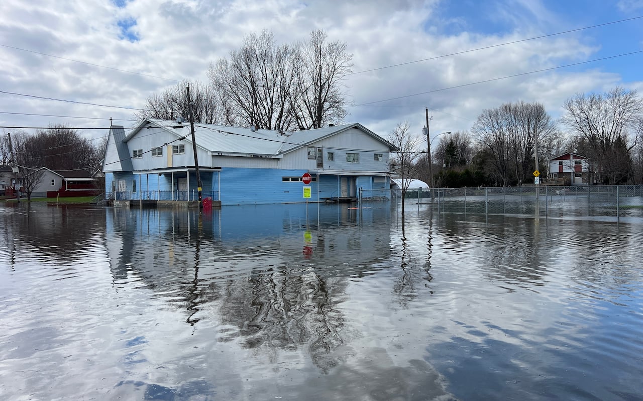 A blue single-storey building surrounded by low floodwaters on a spring day.