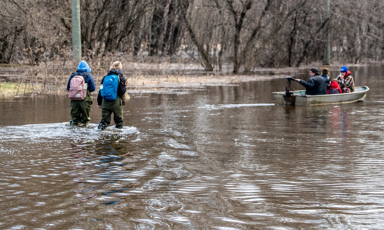 Two people walking through knee-deep water, while two people are on a motor-boat.