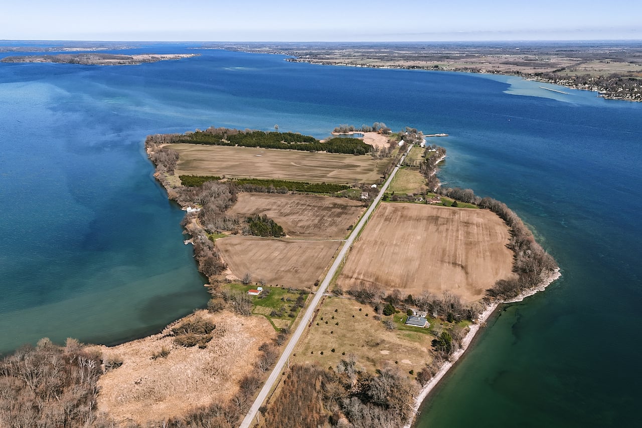 An aerial shot of a small island with one long road and brown land surrounded by water of blue and green shades.