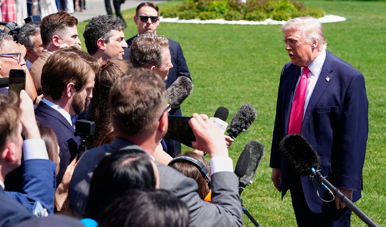 A crowd of reporters, some of them holding microphones, listen to Donald Trump.