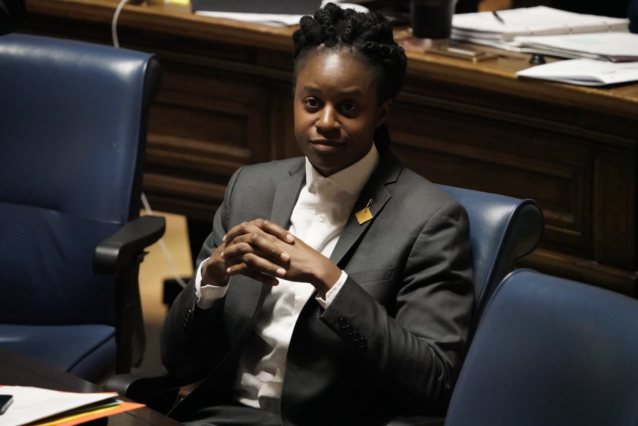A person in a suit sits with hands folded in front of their chest.