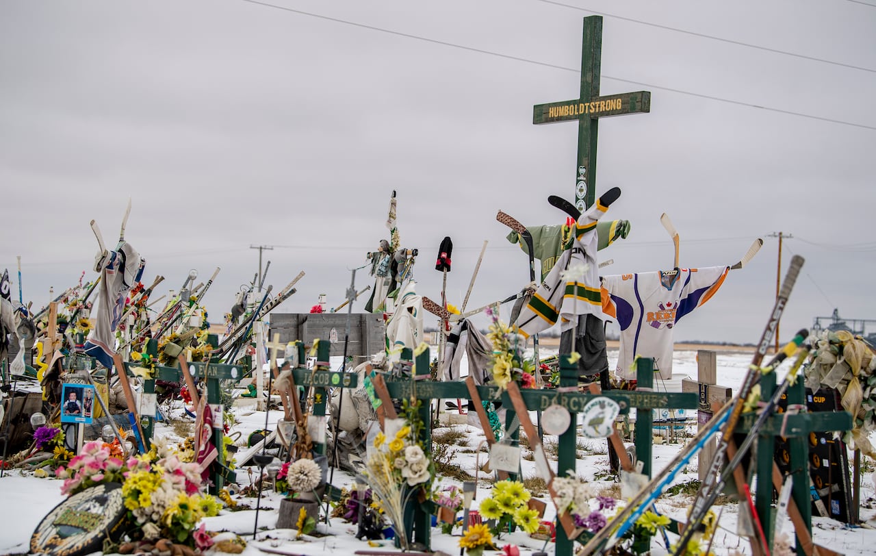 A roadside memorial displays crosses, hockey jerseys and flowers in the snow.