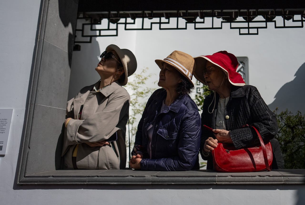 Three women wearing hats look on during a sunny day.