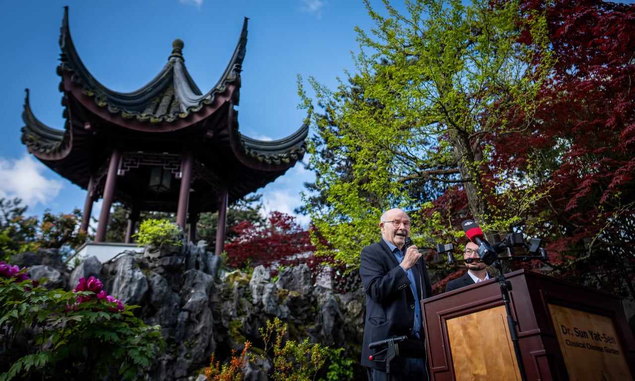 A man speaks at a podium in the shadow of a Chinese-style pavilion.