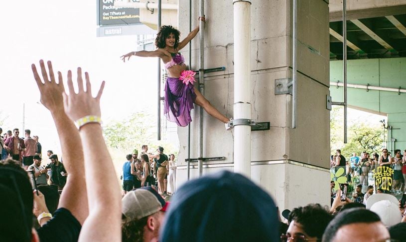 A crowd watches a woman hanging from the side of a support column underneath the expressway.