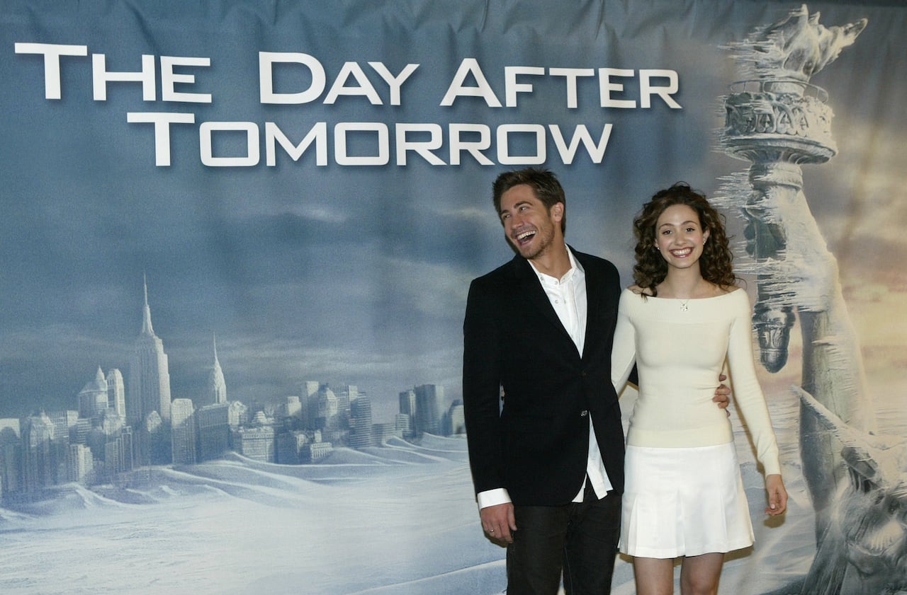 A man and a woman stand in front of a poster where New York City is frozen over.
