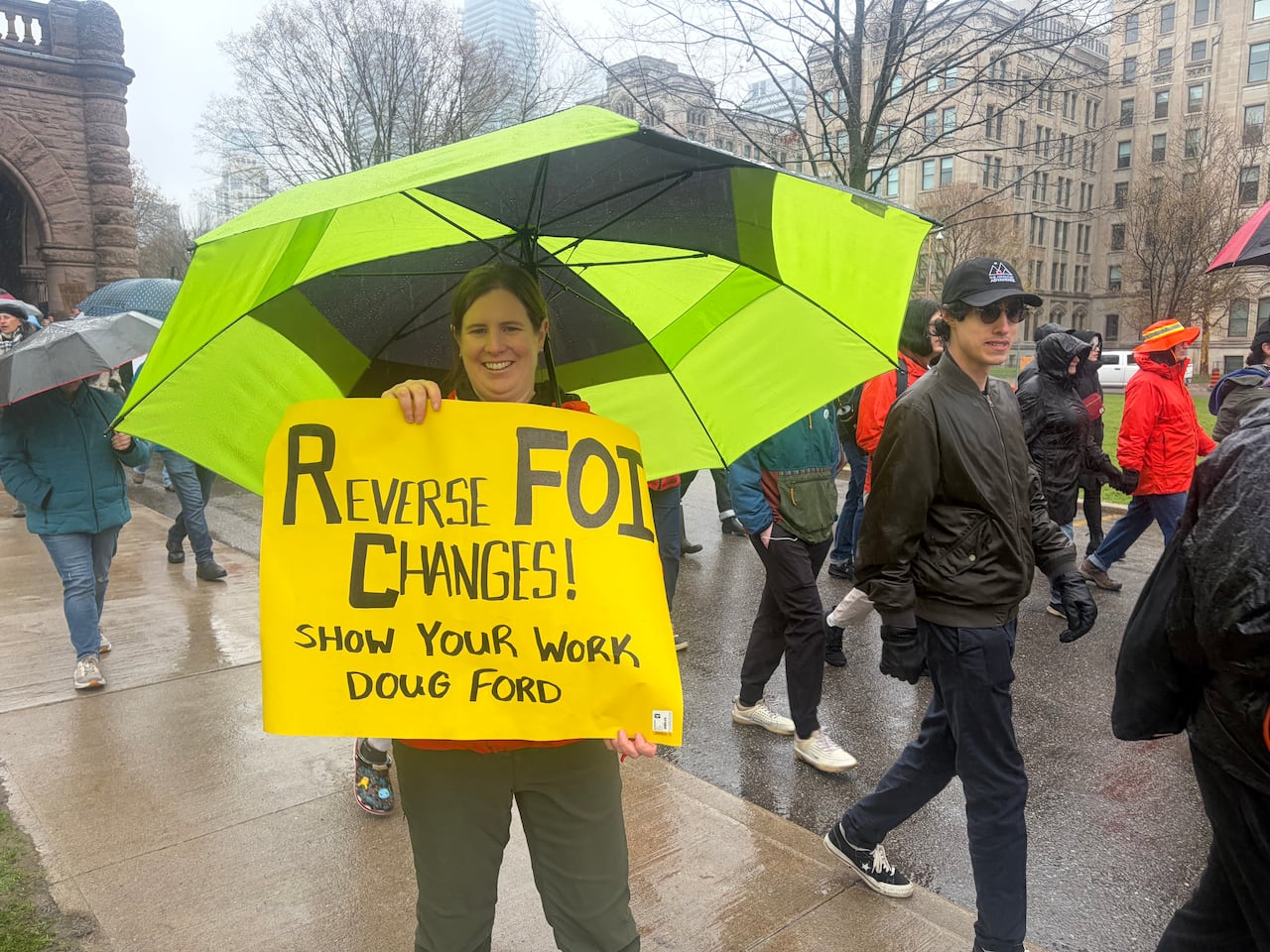 Woman holding yellow sign and umbrella at protest.