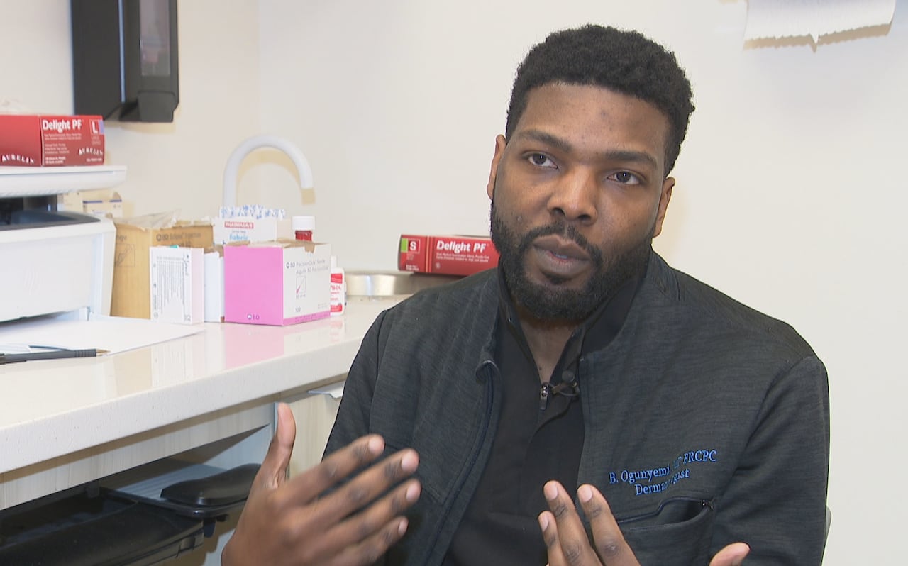 A man in his thirties sits in a medical office speaking with a reporter