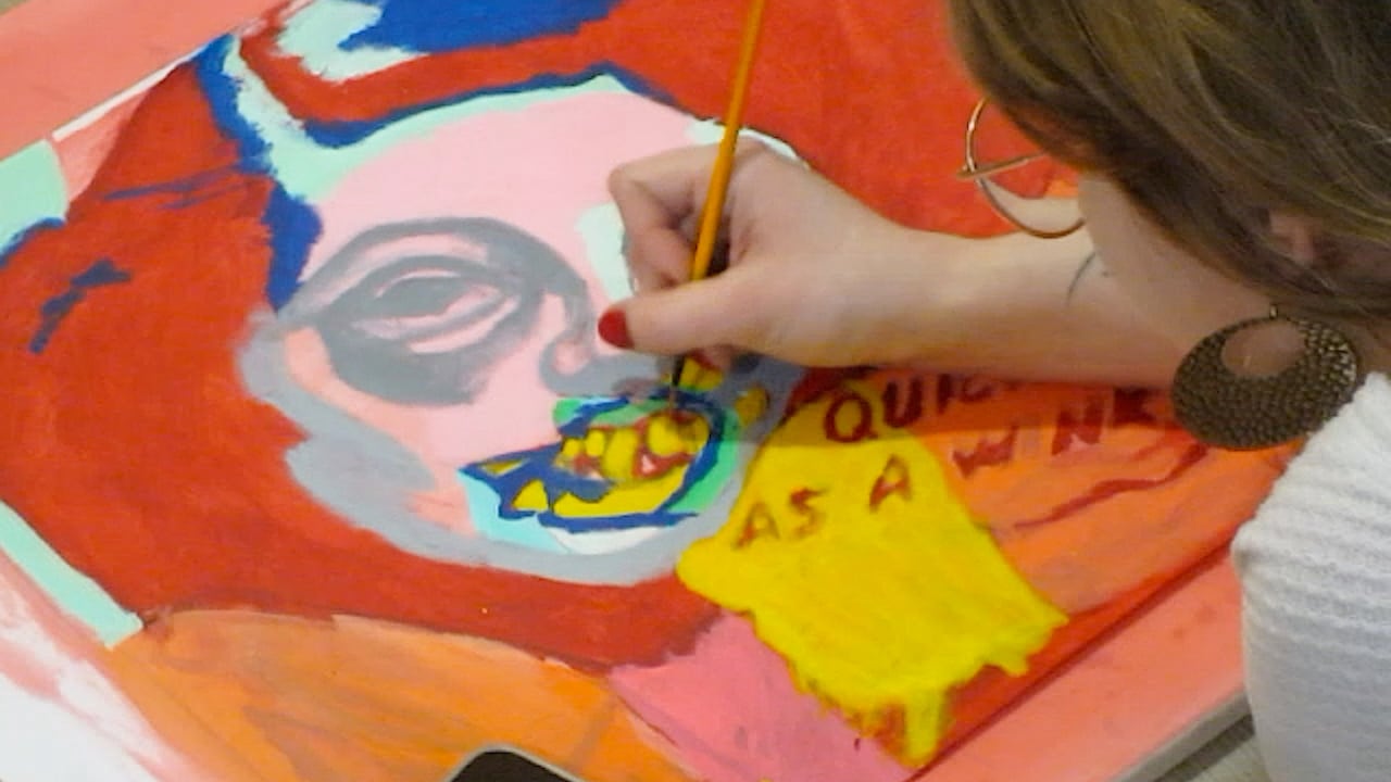 A collage painting with orange and red and a face with yellow teeth.