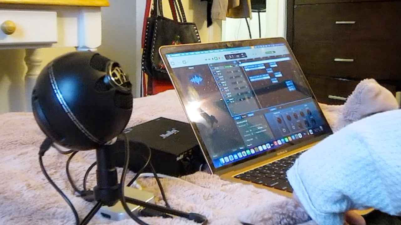 A laptop and microphone sitting on a bed in a home-based recording studio.