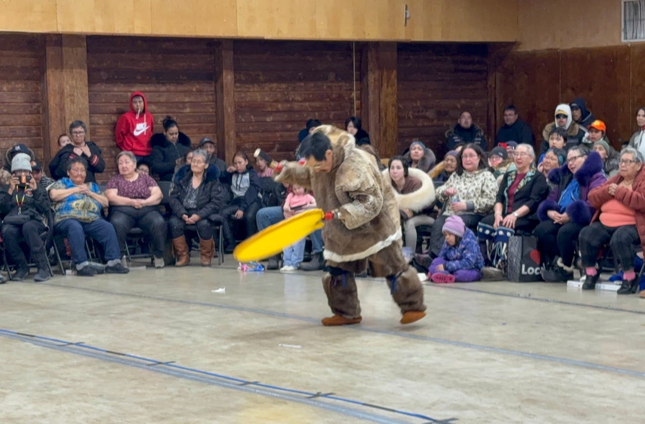 An Inuit drummer performs in front of a group of people.