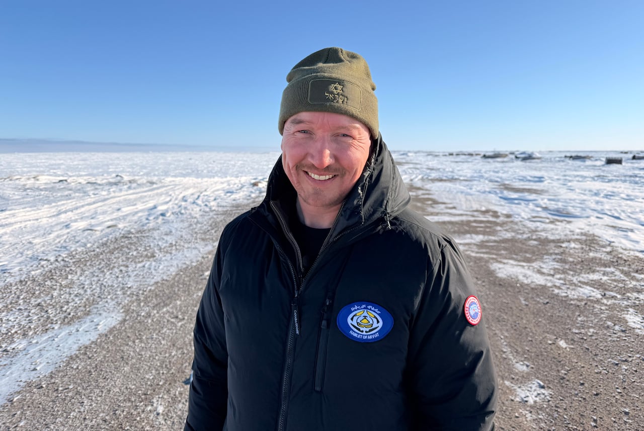 A man wearing a black jacket and a green cap stands on frozen land.
