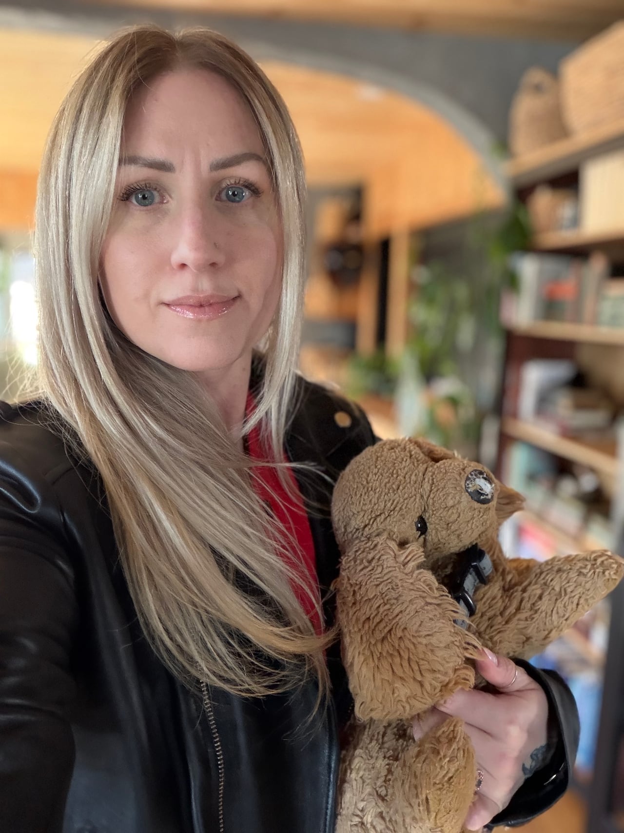 A blonde woman taking a selfie with a concerned face, while holding her daughter's dog stuffed animal.