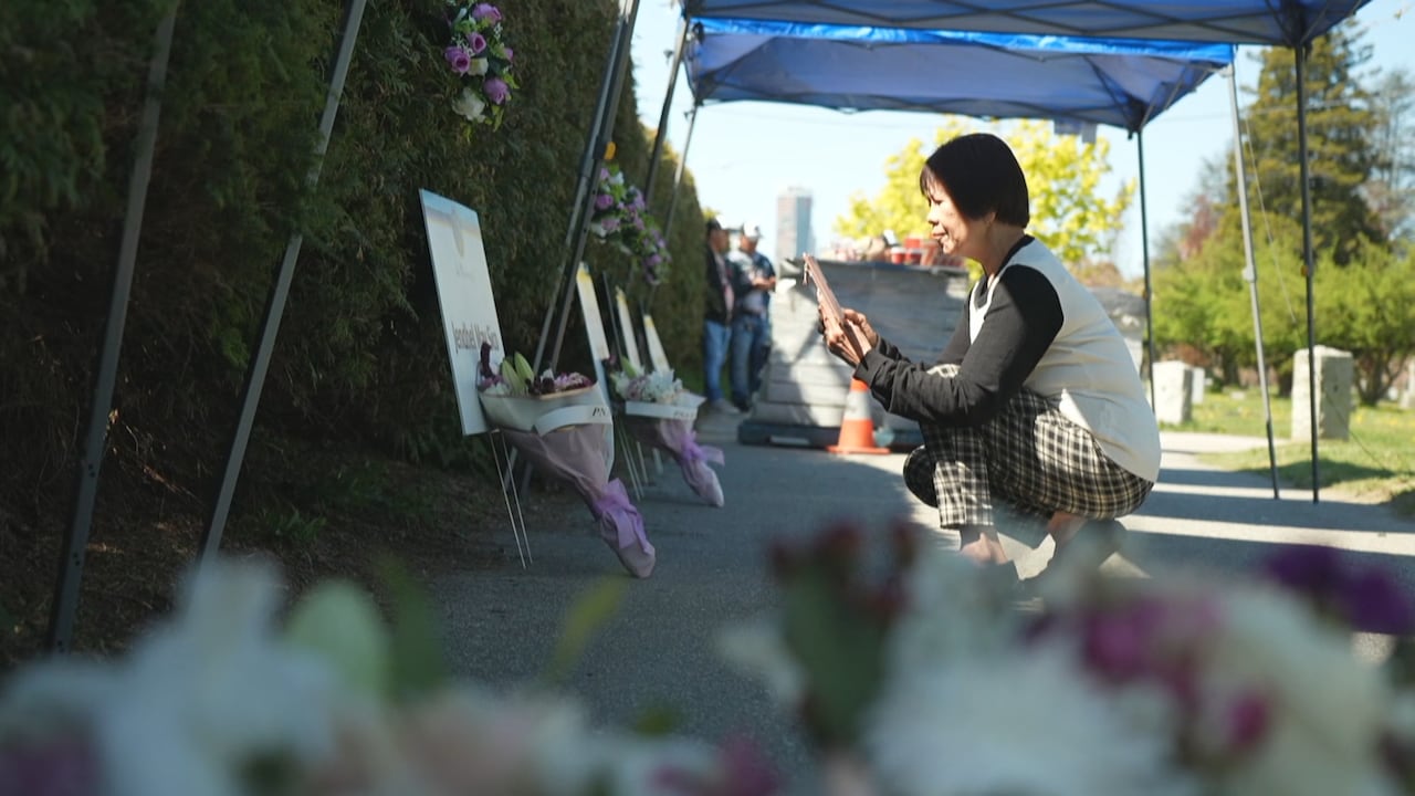 A woman kneels down in front of a row of memorial displays and flowers.