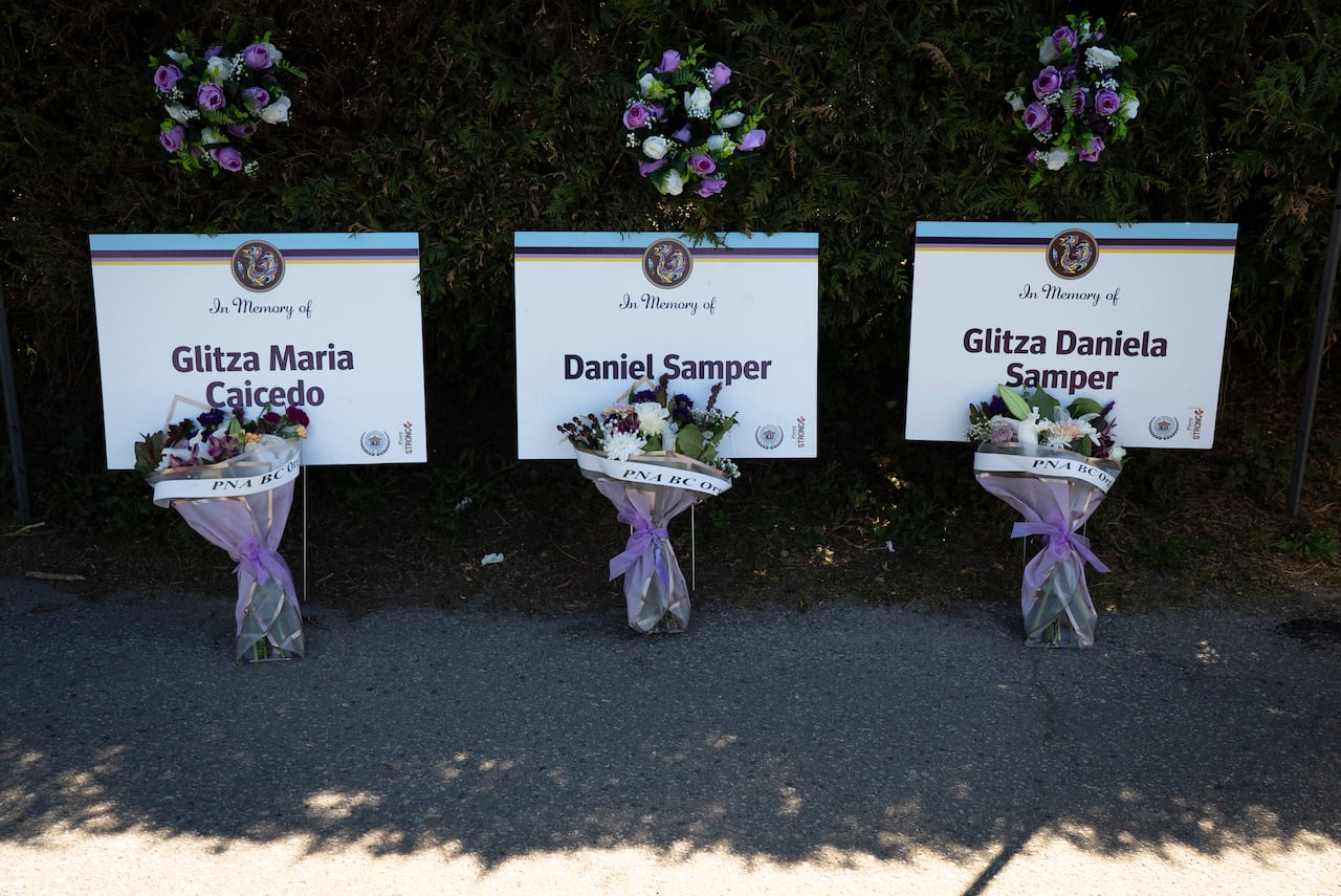 Signs with names and bouquets of flowers are placed along a hedge, honouring individuals in a memorial display.