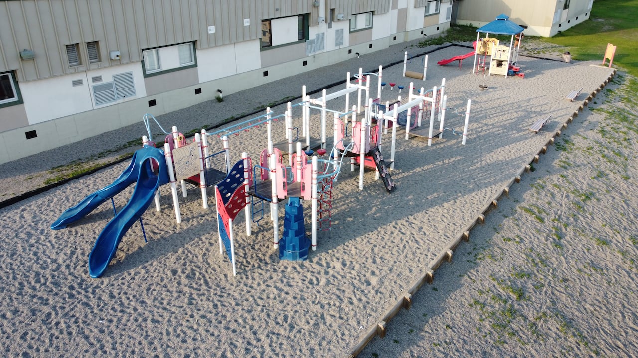 An aerial shot of a blue a red playground in front of a white school building.