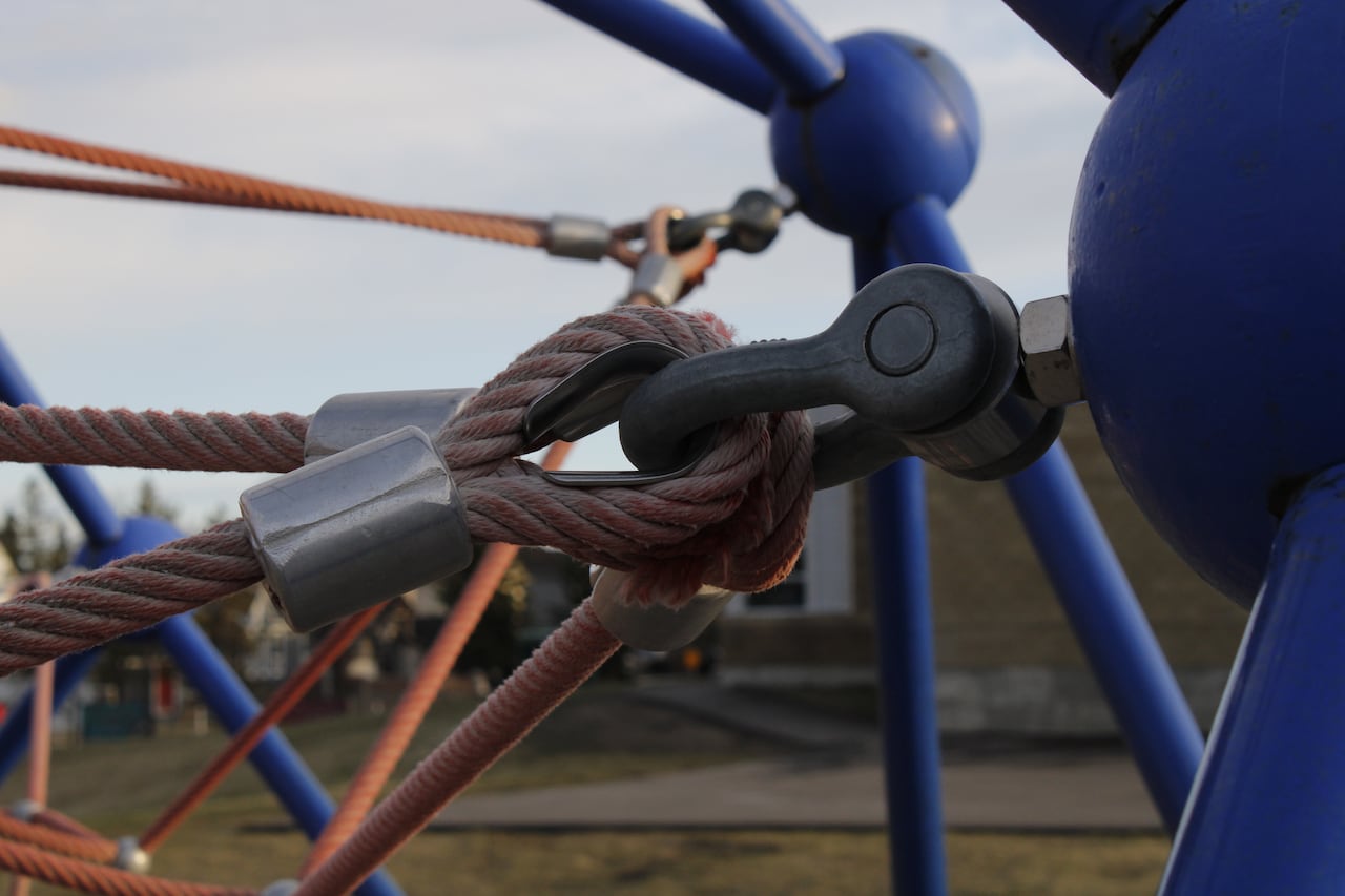 A close-up of a fraying rope on a climbing structure at a school playground.