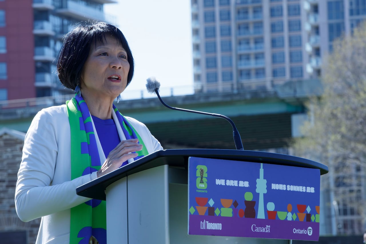 A woman stands at a podium and speaks into a mic, with a condo behind her.