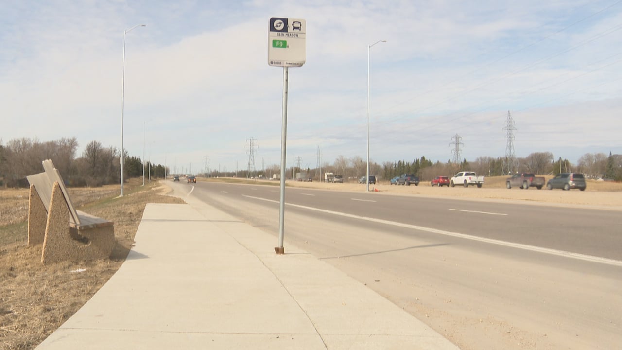 A bus stop sign and a bench by a road, with cars coming toward them.