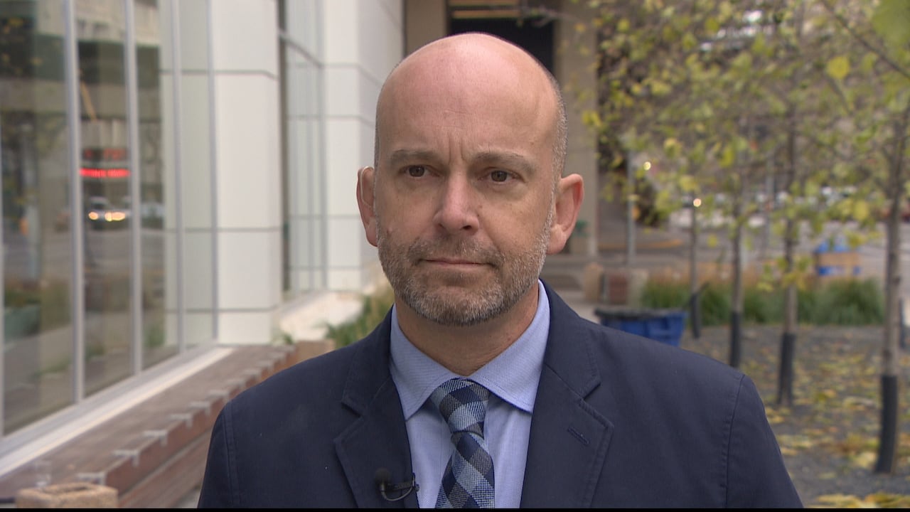 A man in a dark suit and tie speaks with a reporter.