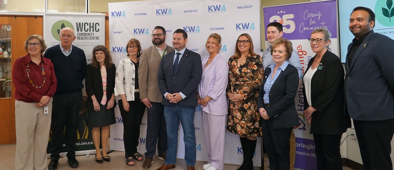 A group of men and women in professional clothing stand in front of healthcare-organization themed banners.