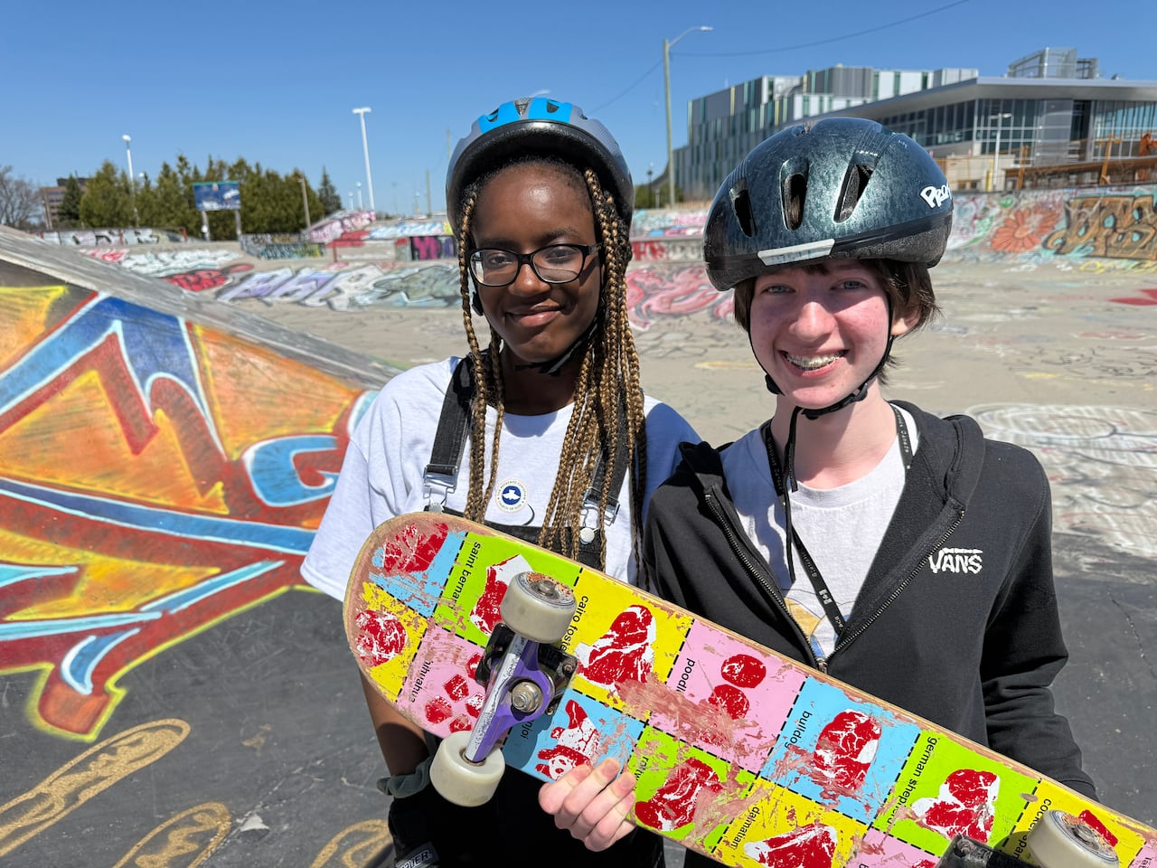 Two young skateboarders wearing a helmet and brandishing a skateboard at a park