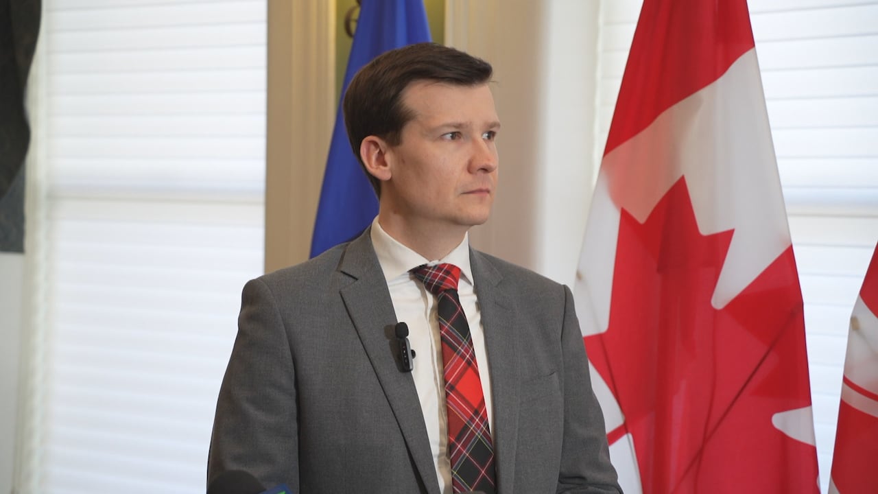 A man standing in front of the Canadian flag looks off camera.