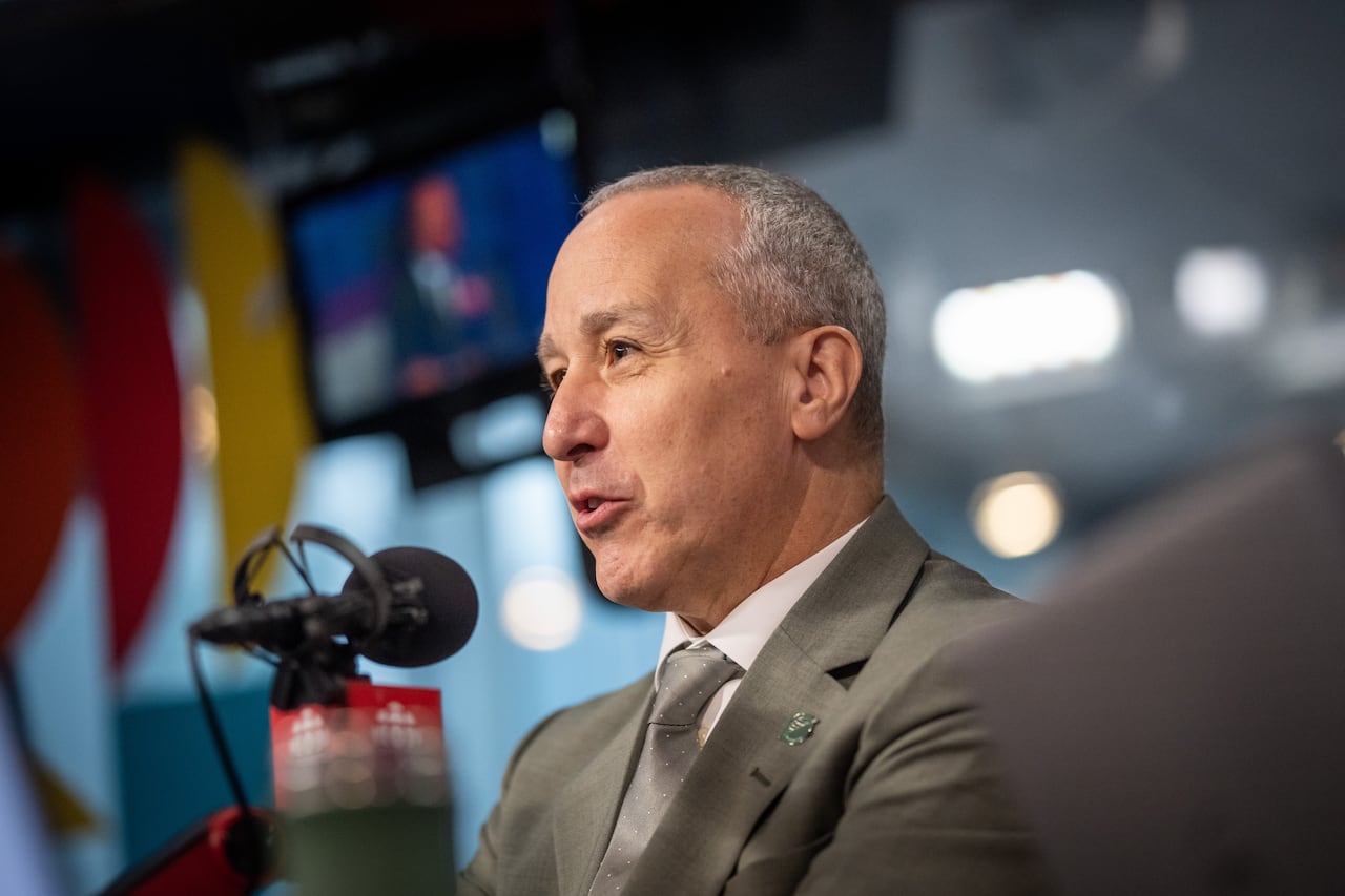 A man in a suit with grey hair sits at a microphone in a radio studio.