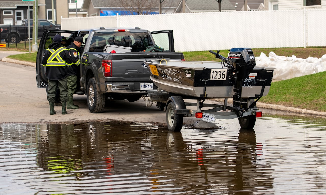 Two firefighters in rubber boots near a truck with a boat attached to it.