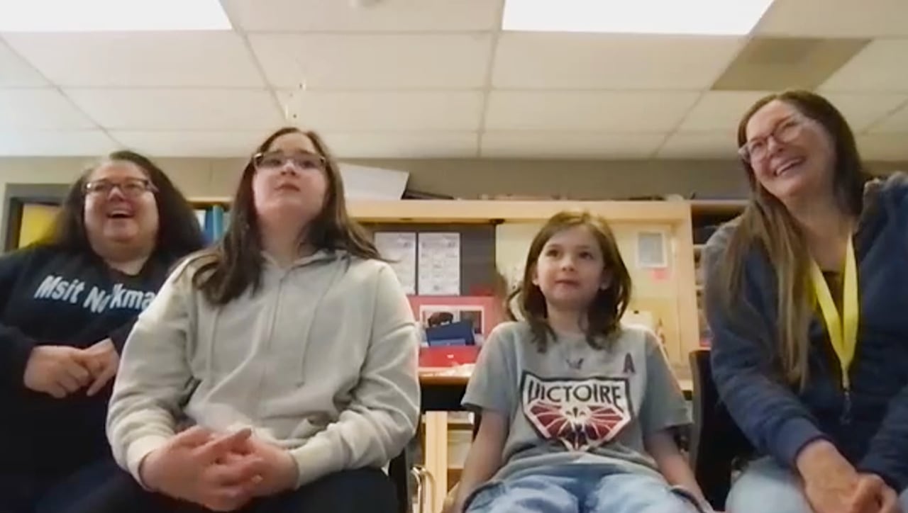 A Zoom screenshot of a family sitting in a line in a classroom