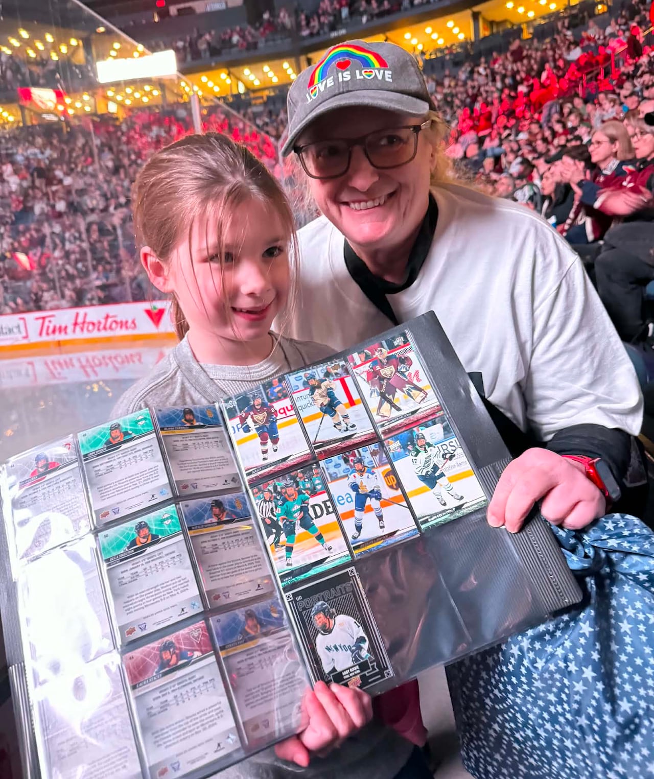 A young girl sitting next to an adult woman. They are holding an open book of hockey cards.