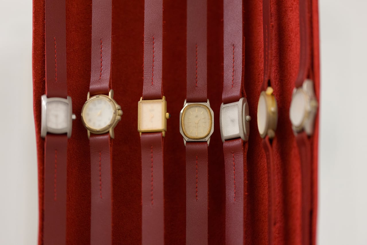 The close-up photo shows seven wristwatches with red leather straps. The face of each watch is too fogged to read the time.