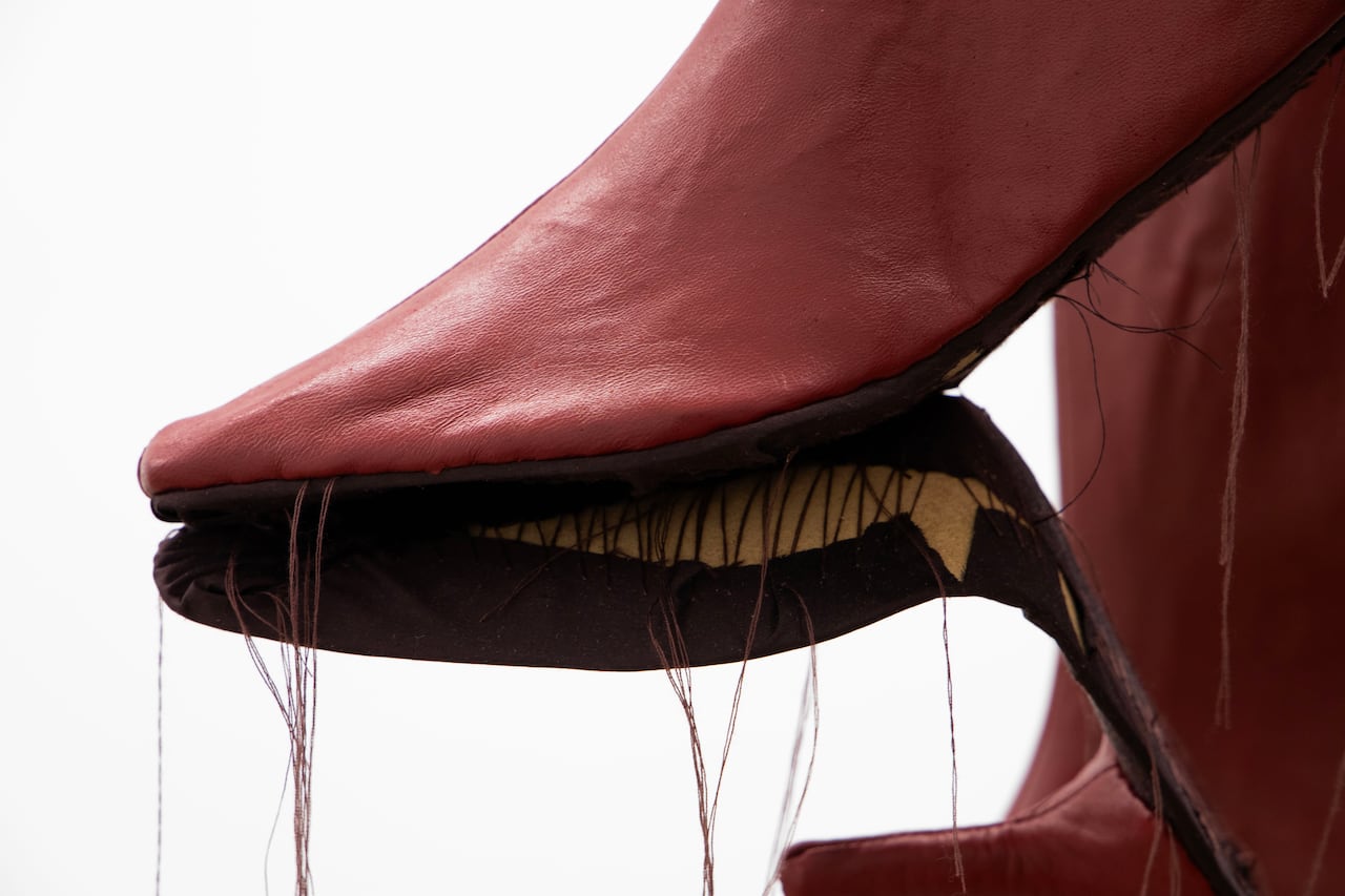 The close-up photo shows the foot of a red leather boot. A component of its constructions hangs off the boot with threads dangling.