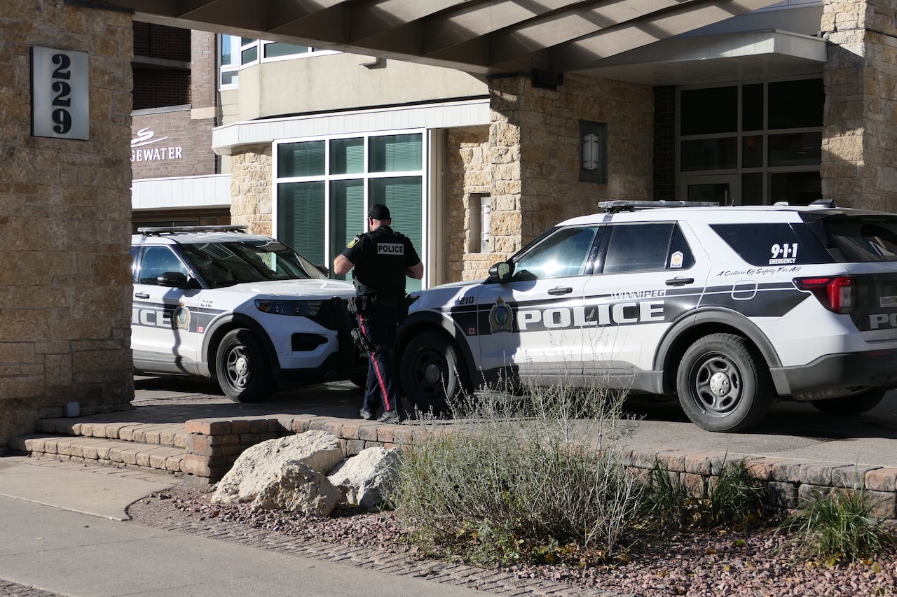 A police officers walks between two vehicles parked outside a residential building's entrance.