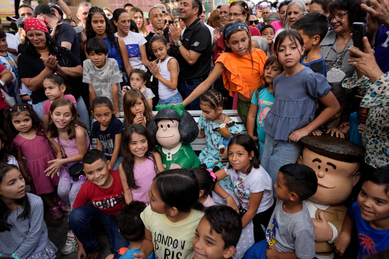 Children and people surround a sculpture of Argentine cartoon strip character Mafalda, during its inauguration commemorating the 50th anniversary of the last strip published in a newspaper, at Oberón square in Caracas, Venezuela, Sunday, June 25, 202