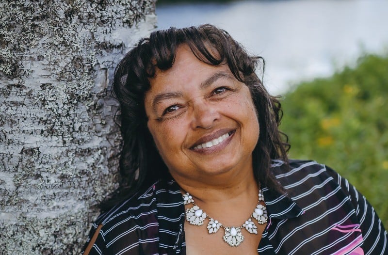 A woman wearing pink and black leaning against a tree.