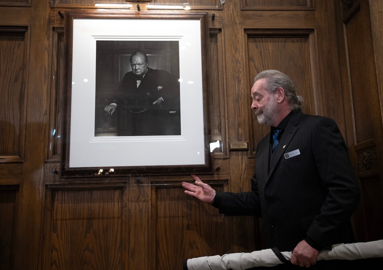 A man stands next to a portrait on the wall.