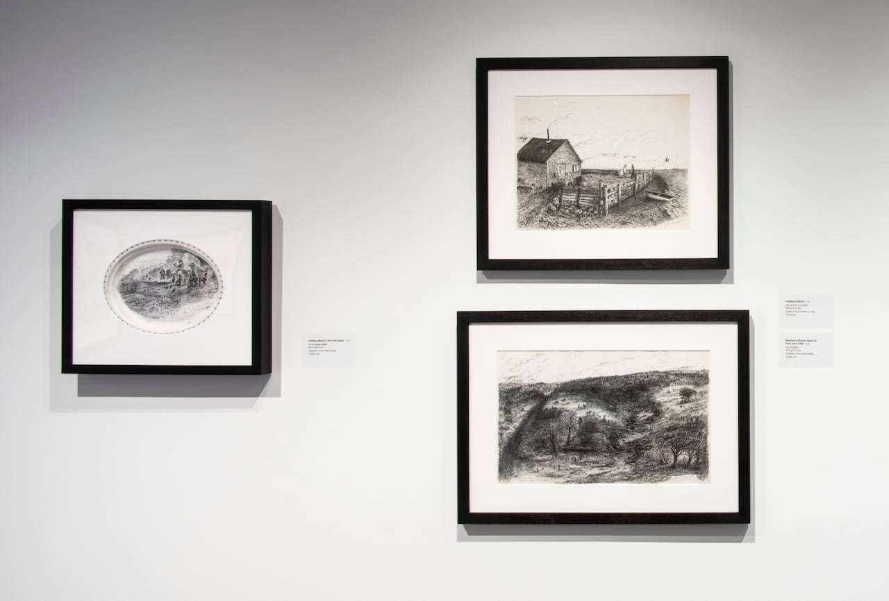 Three ink drawings, one of a group of people, another of a cabin, a third of people picking blackberries, all mounted on a white wall.