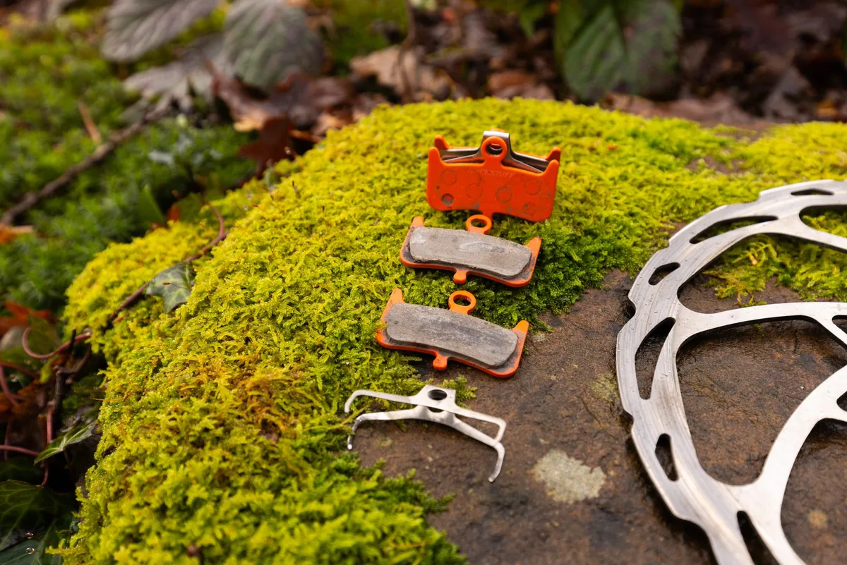 Trickstuff Power brake pads and spring laid out on moss next to a disc brake rotor