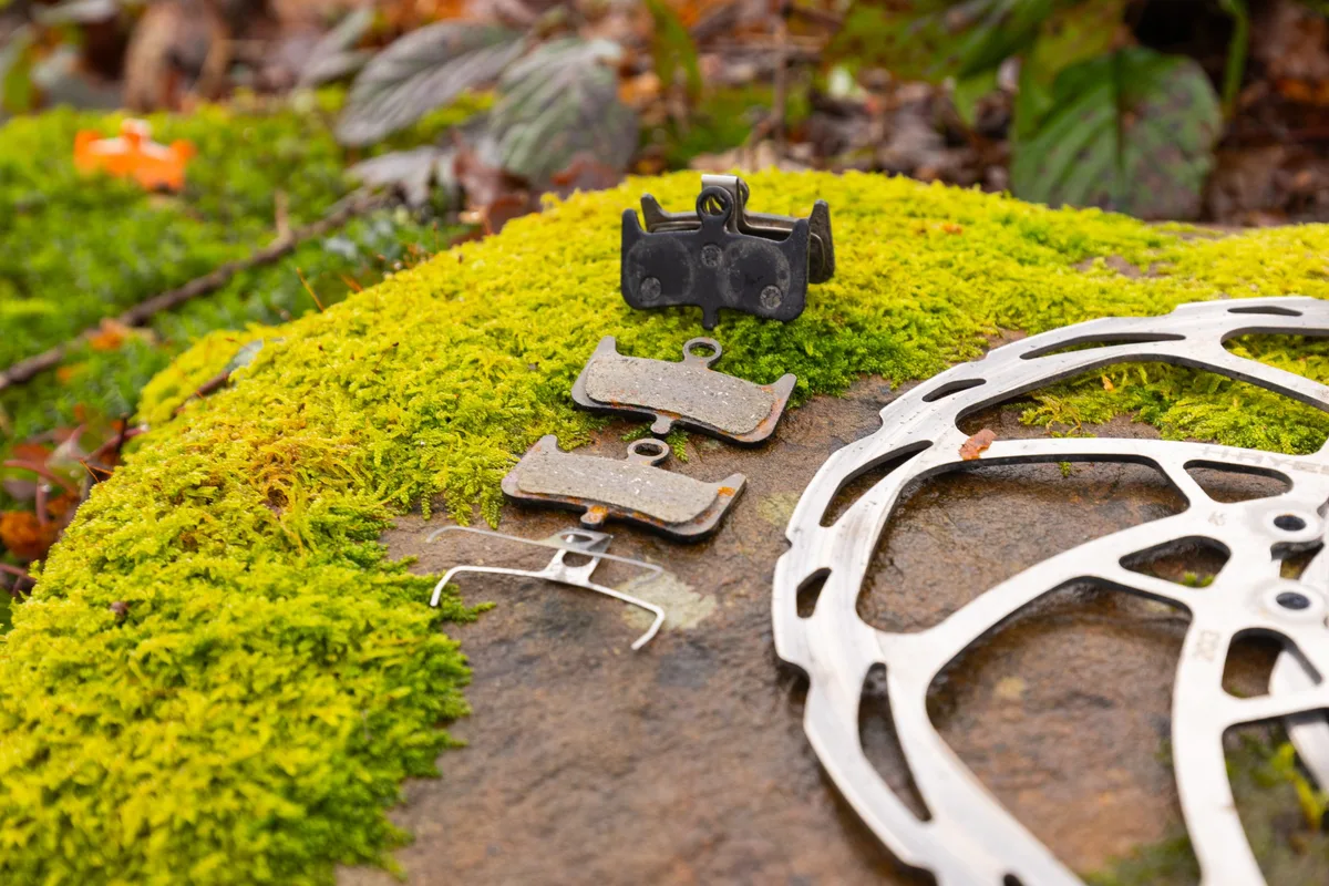 AliExpress Kingstop brake pads and spring next to a mountain bike disc brake rotor on a mossy rock