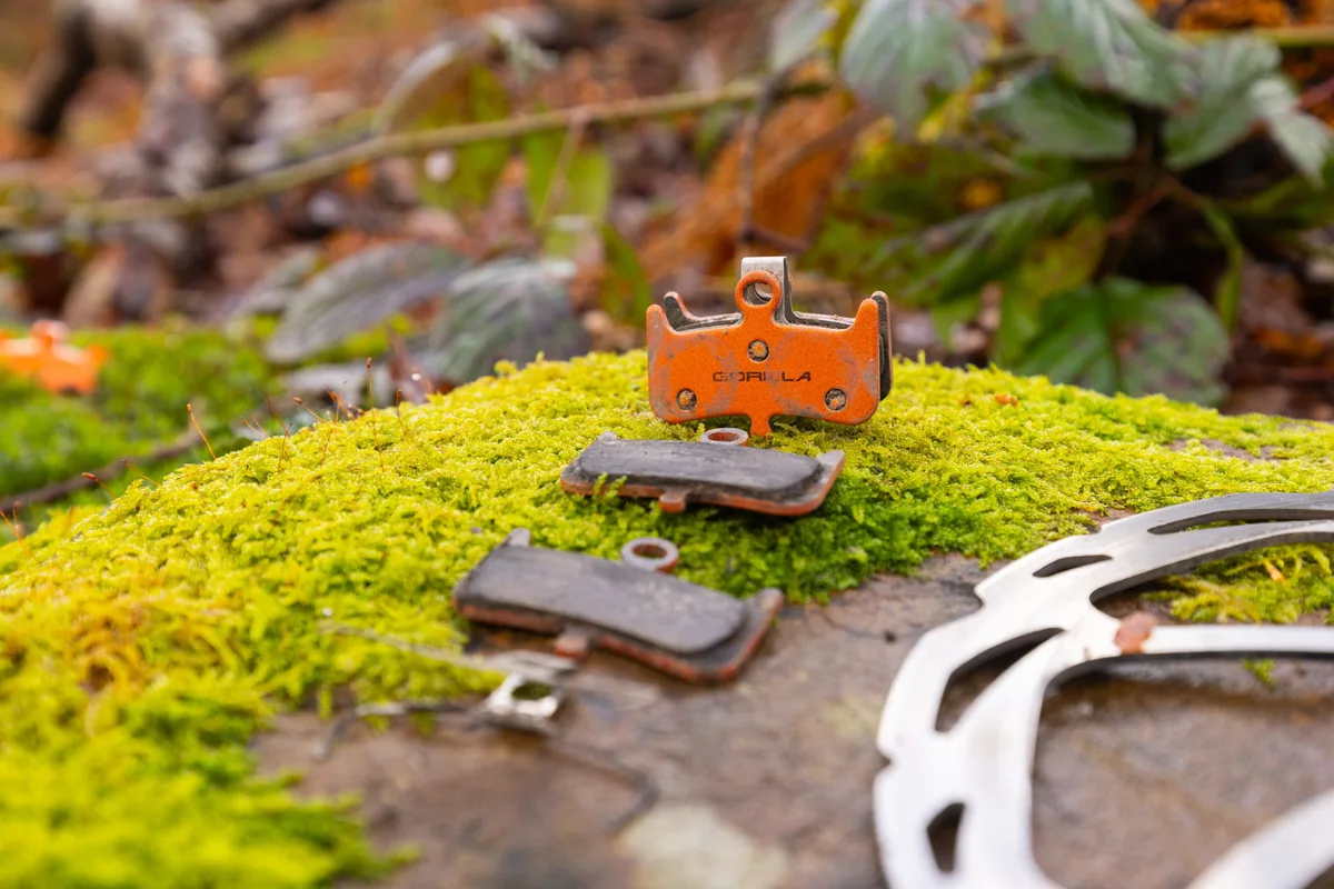 Gorilla Enduro Pro brake pads and spring positioned on a mossy rock beside a disc brake rotor