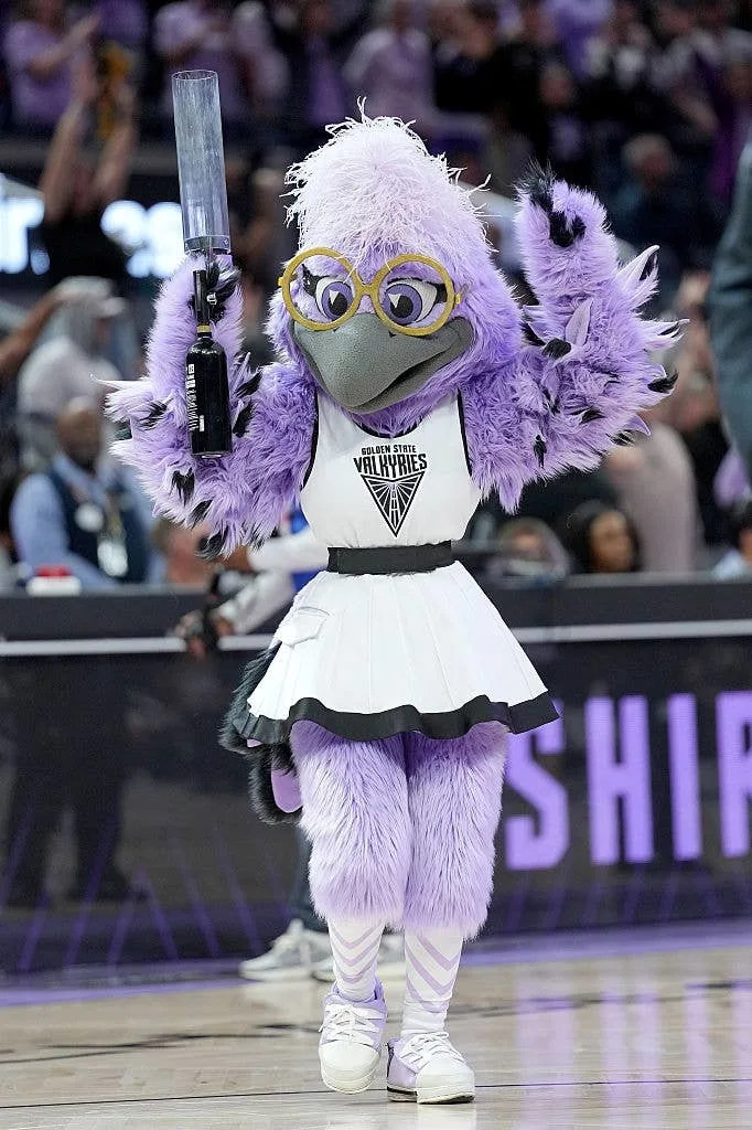 A sports team mascot in a cheerleader outfit performs on a basketball court, energizing the crowd during a game