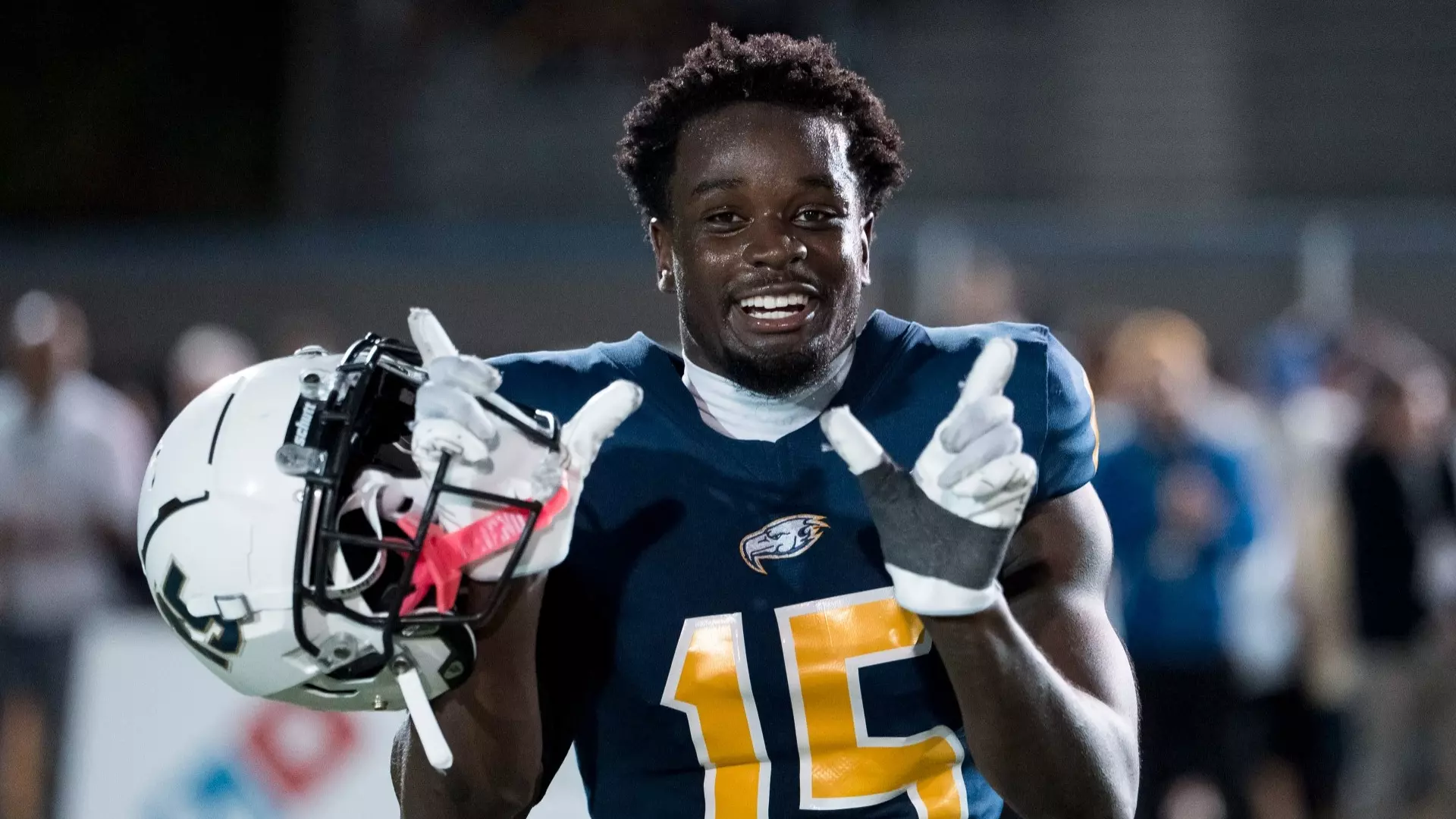 Ben Sangmuah with his helmet off, grinning directly into the camera in semi closeup, making a W sign with his two hands to celebrate the UBC Thunderbirds win over the Calgary Dinos