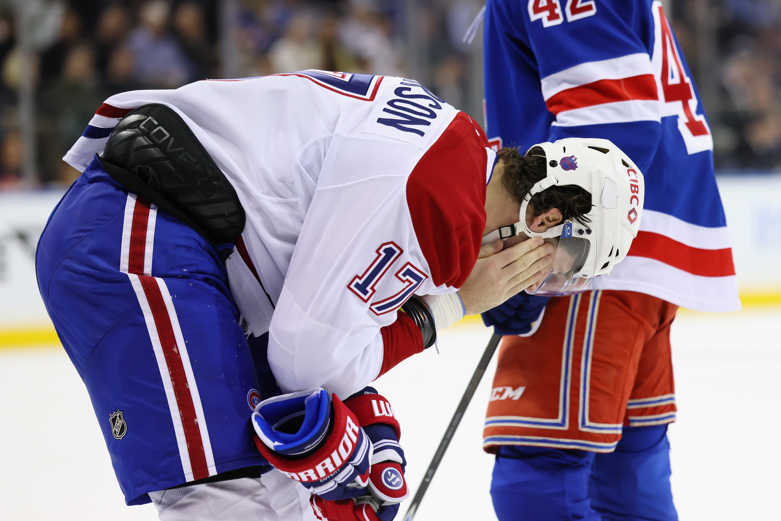Hockey player hunches over holding a hand to his face after being hit by the puck.