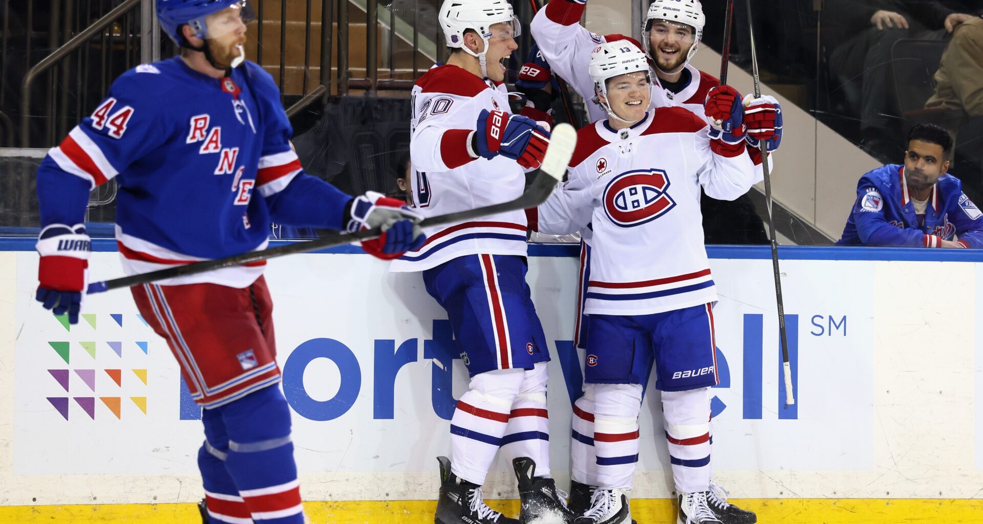 Hockey players gather to celebrate the winning goal as an opponent stands nearby looking dejected.