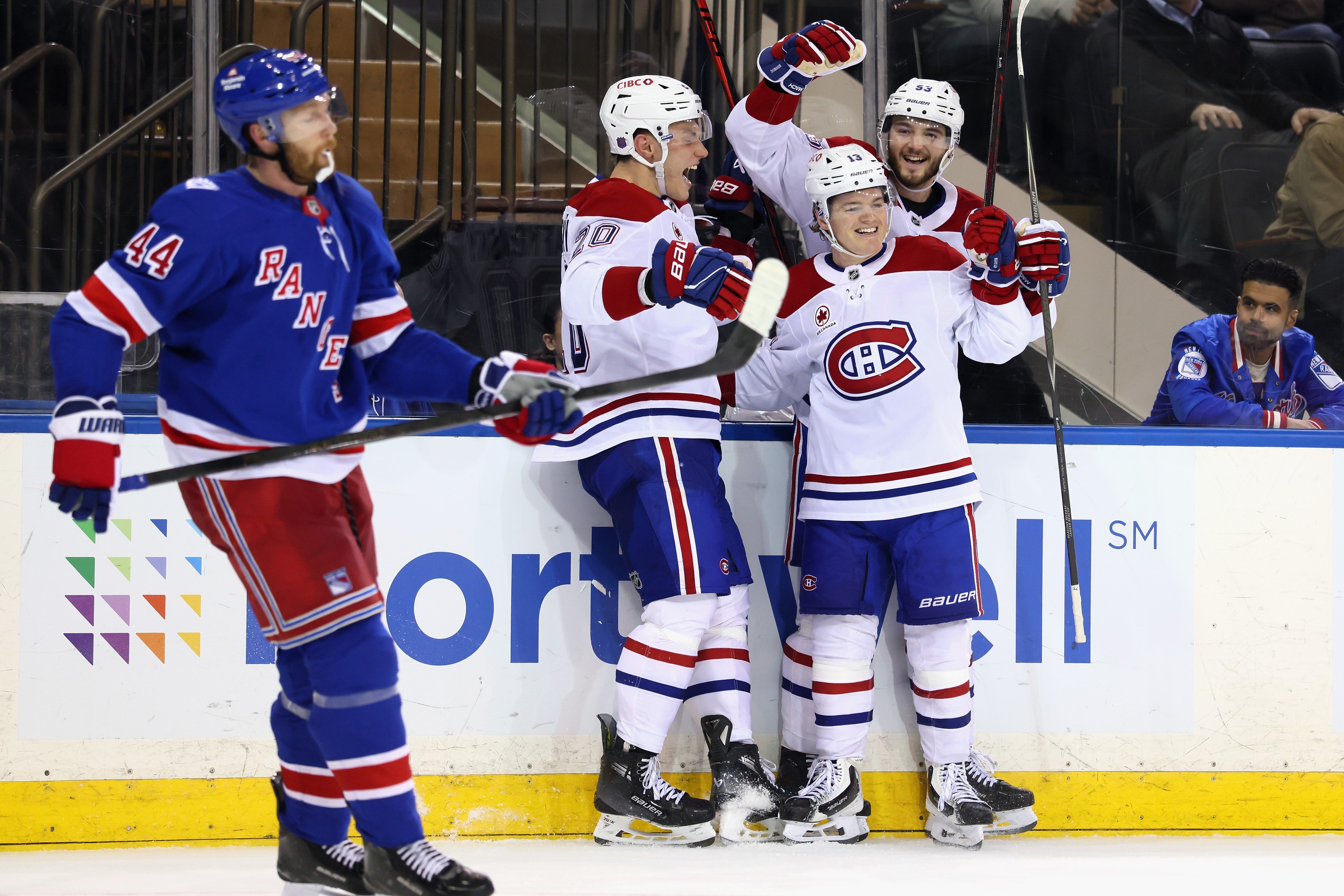 Hockey players gather to celebrate the winning goal as an opponent stands nearby looking dejected.